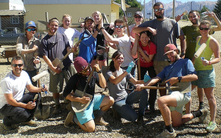 A group of people holding paint brushes pose for a group photo during a service project with outward bound.